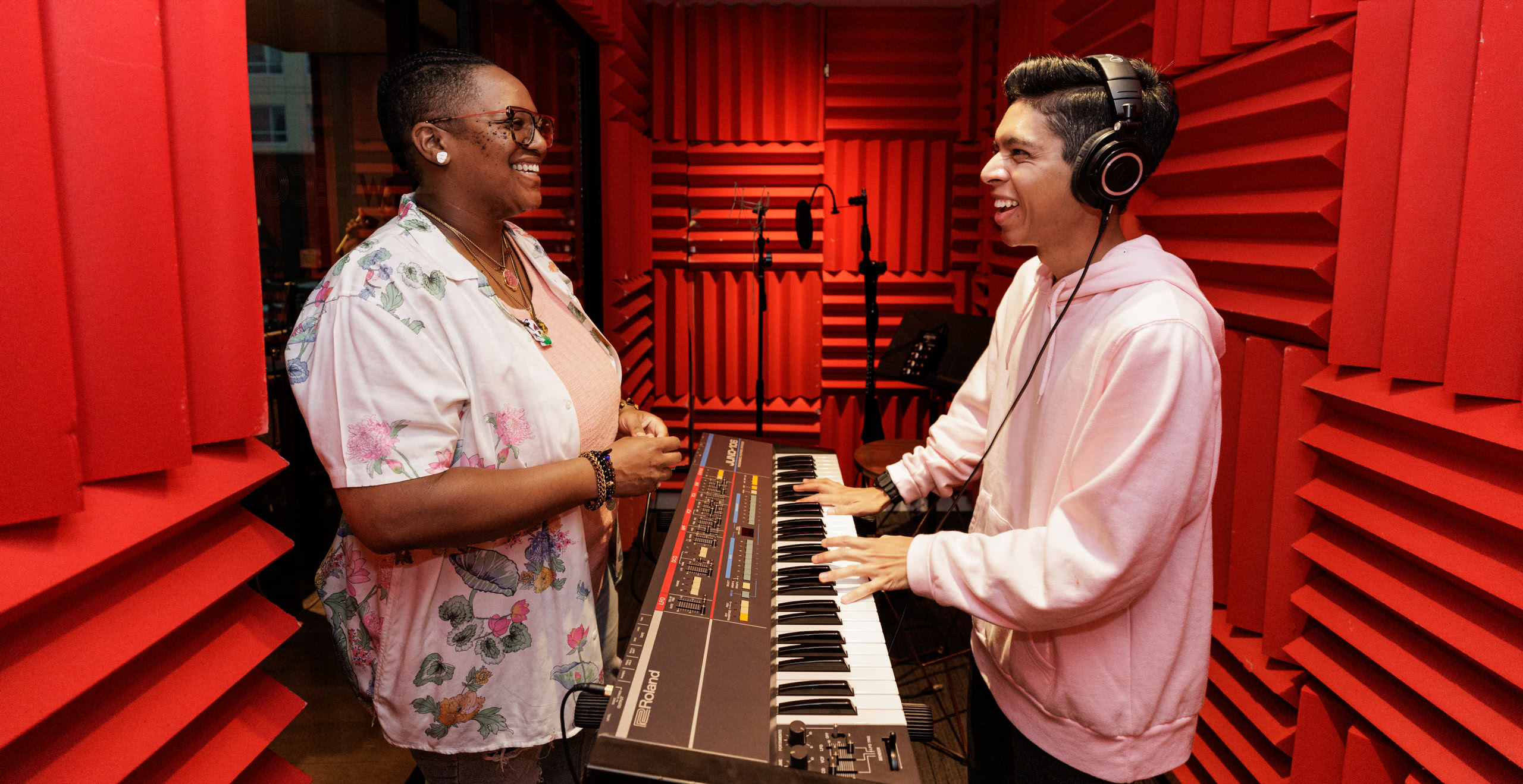 Young man playing keyboard with producer in music studio.